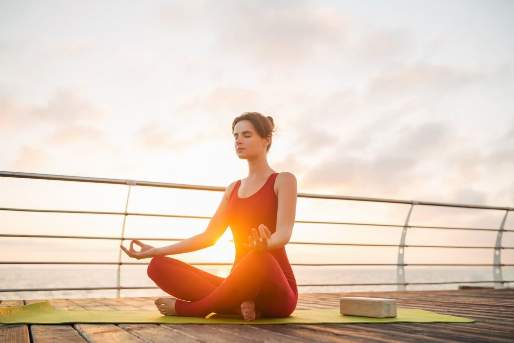 young slim beautiful attractive woman doing yoga in the morning on sunrise by sea, healthy lifestyle
